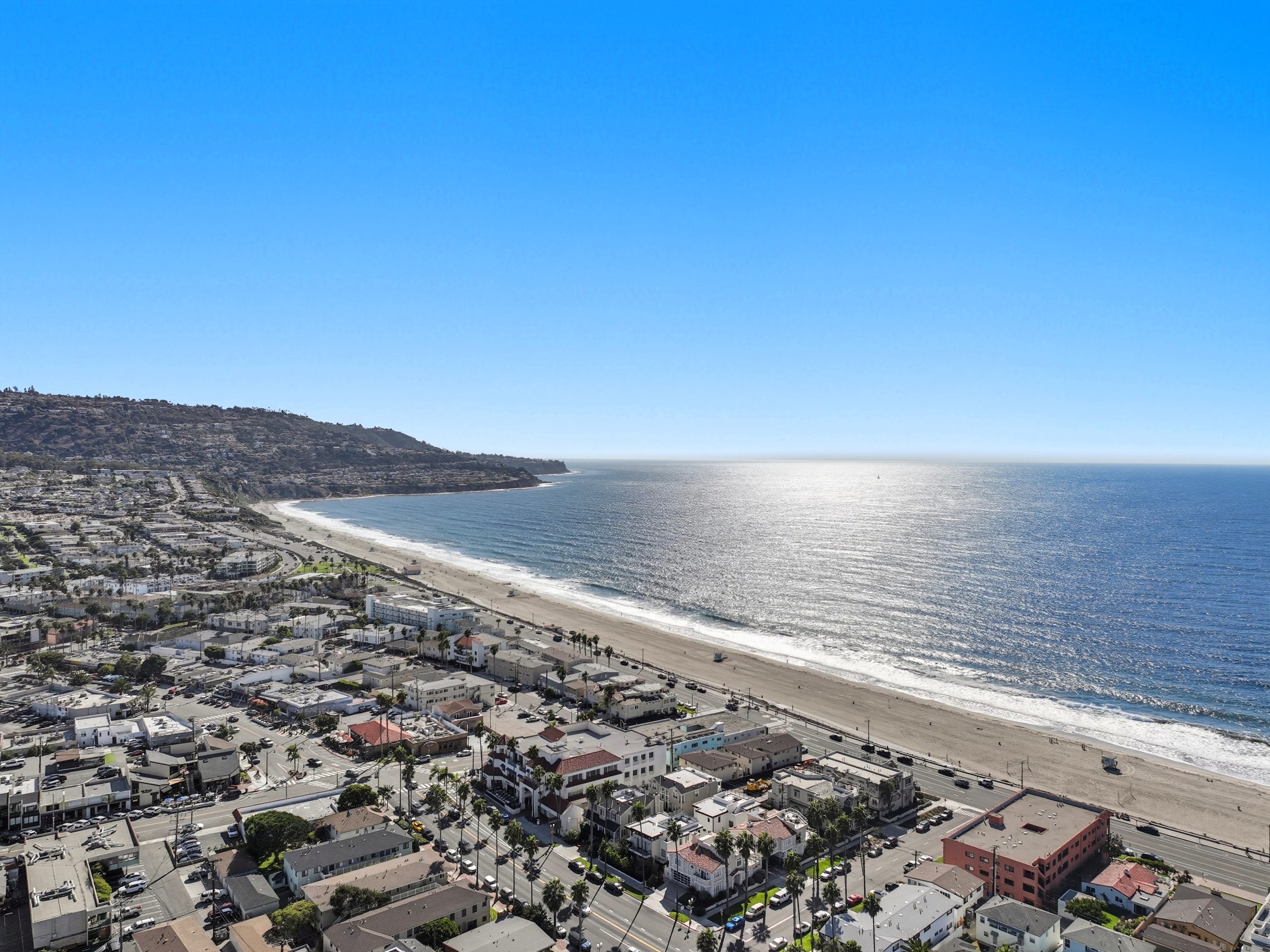Aerial looking south along the beach with sun on the water and the Palos Verdes Peninsula rising at the end of the bay
