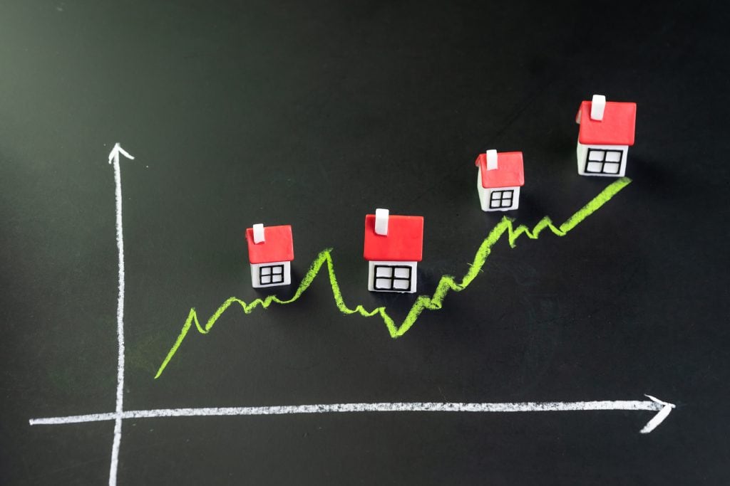 A rising chalk line drawn on a blackboard with four small model houses climbing along it