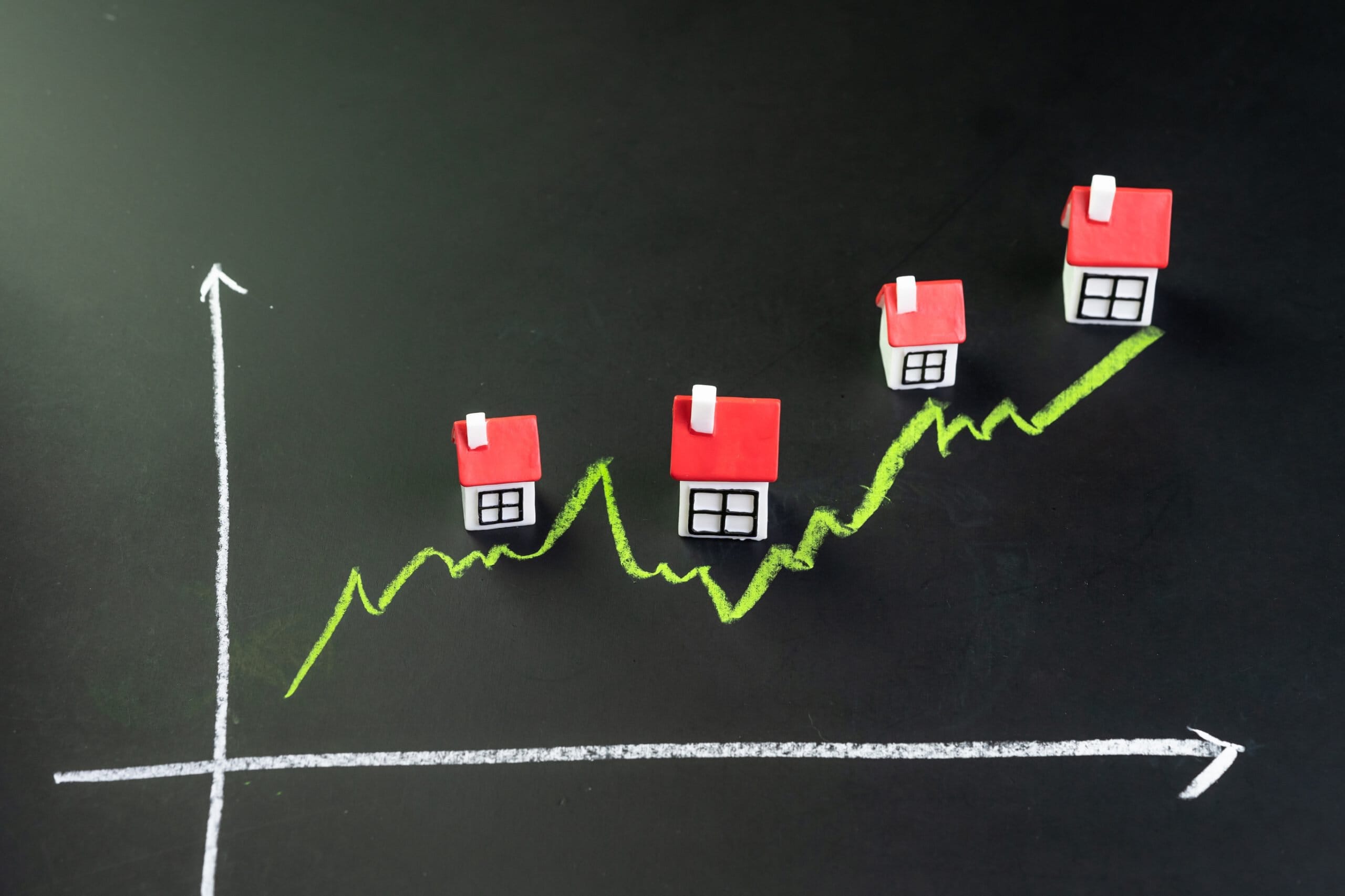 A rising chalk line drawn on a blackboard with four small model houses climbing along it