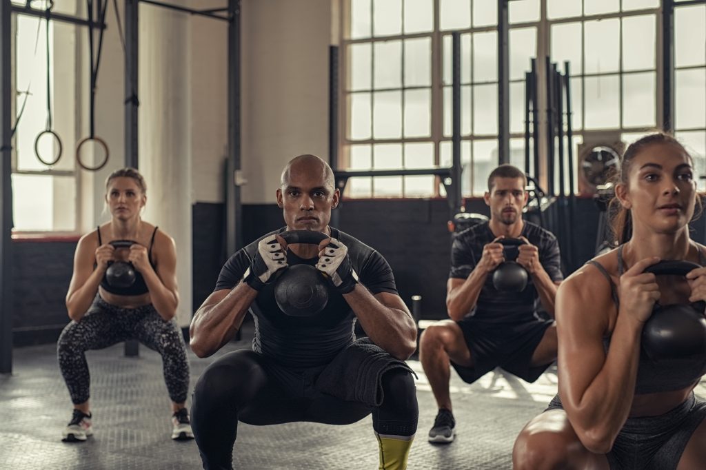 A group fitness class performing a squat with dumbbells in a studio