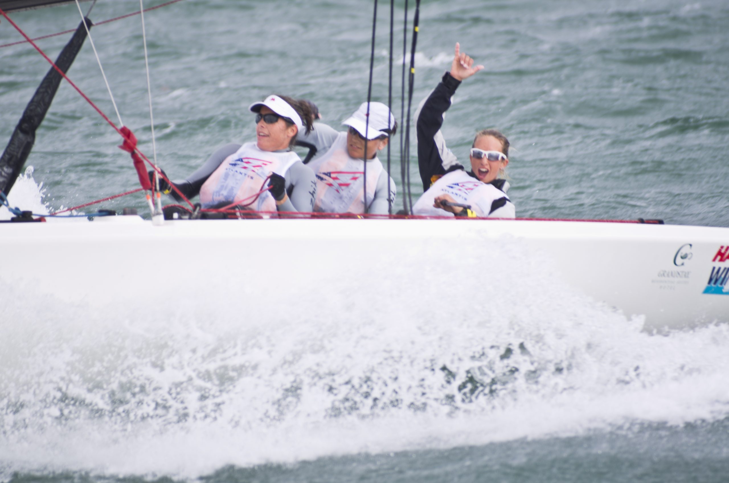 Crew hiking out over the rail of a racing sailboat through spray