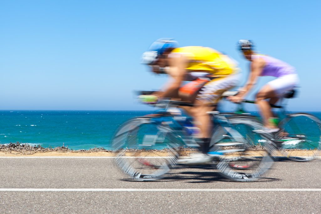 Two cyclists riding along a coastal road with the ocean behind them