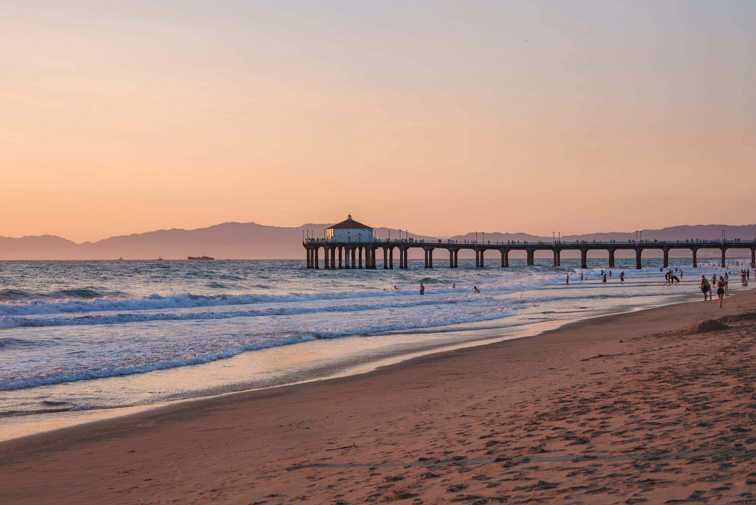 The Manhattan Beach Pier seen along the sand at dusk with the mountains behind