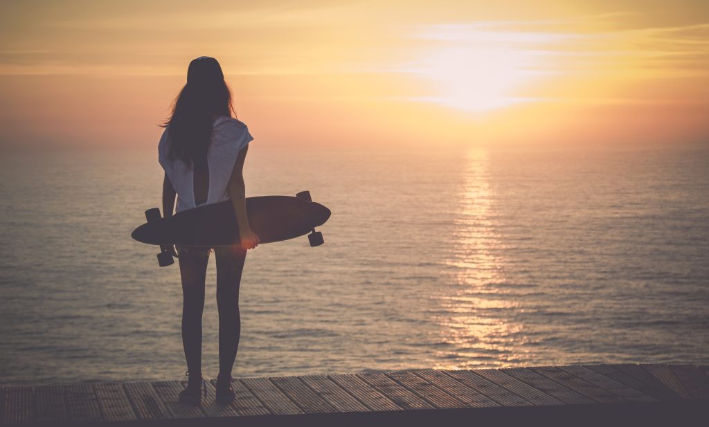 A person holding a longboard skateboard watching the sun set over the Pacific