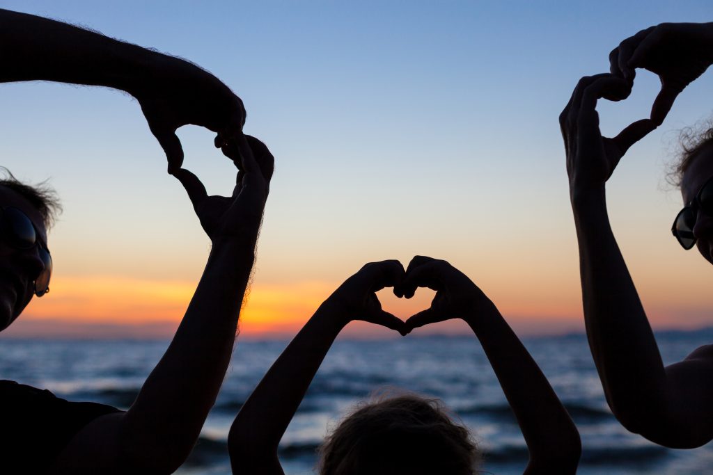 South Bay locals making heart shapes with their hands against a sunset over the ocean