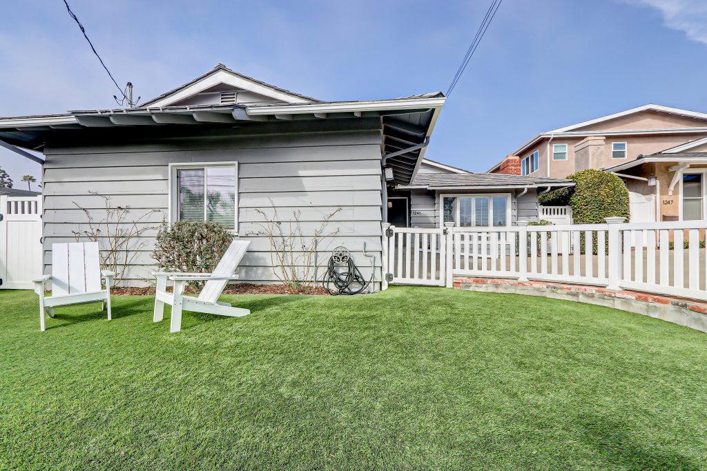 Front lawn of a South Bay home with two Adirondack chairs, enclosed by a white picket fence set on a brick base