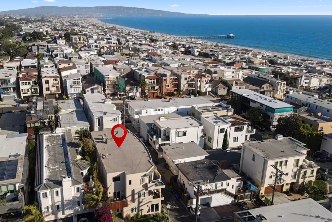 Aerial over the dense street grid of a beach city with the pier and coastline beyond