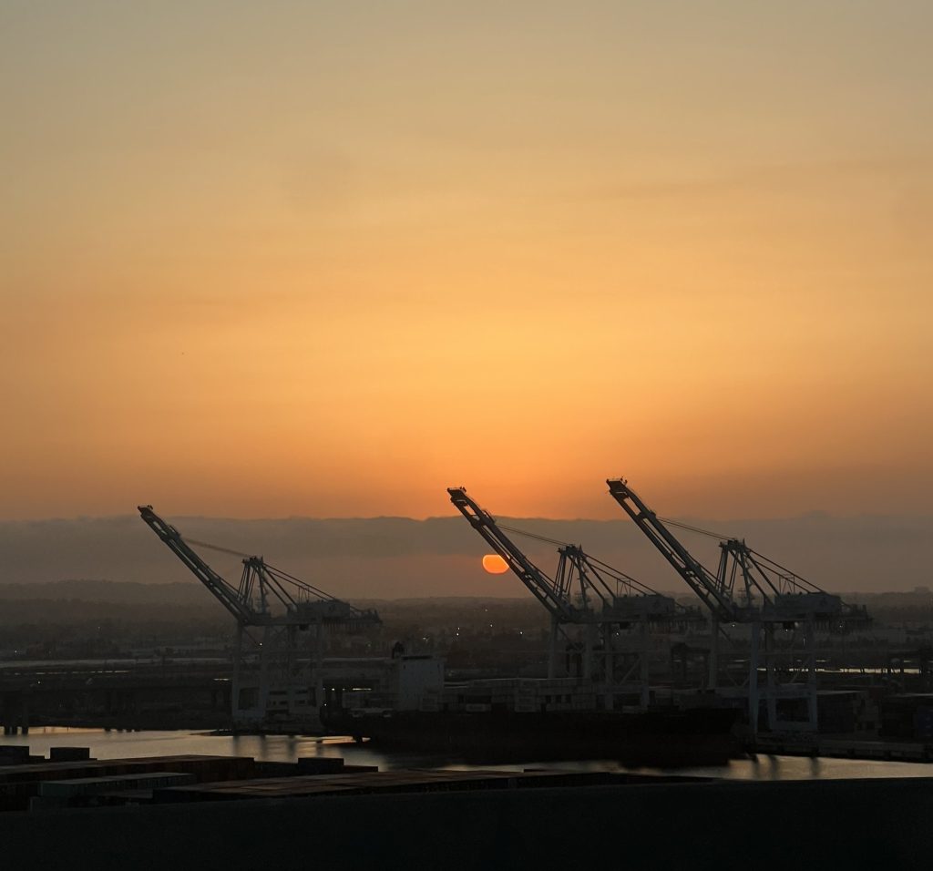 Container gantry cranes against a sunset sky at the Port of Los Angeles