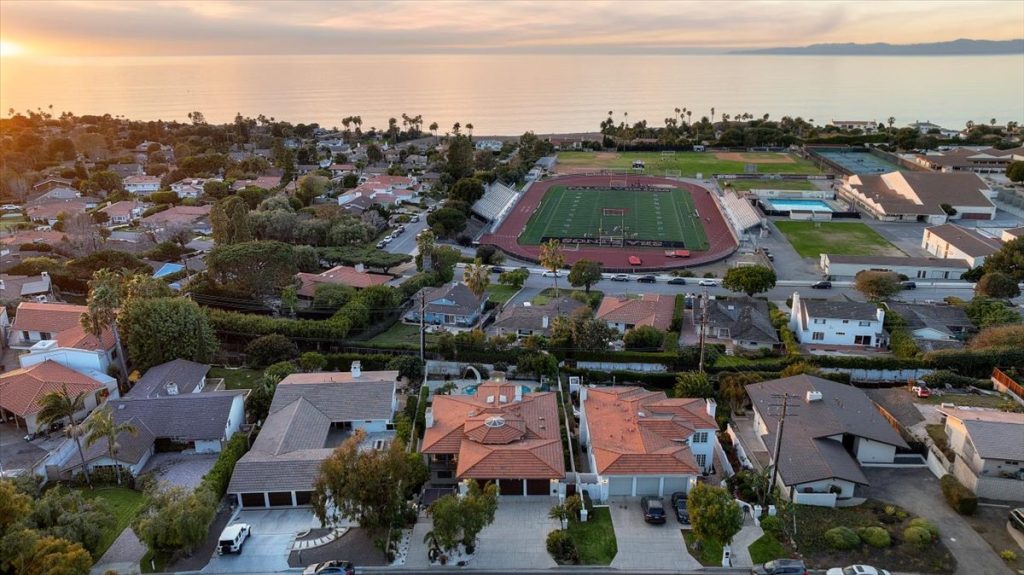 Aerial view at sunset over Palos Verdes Estates: tile-roofed homes in the foreground, the Palos Verdes High School stadium, track and pool behind them, and the ocean on the horizon