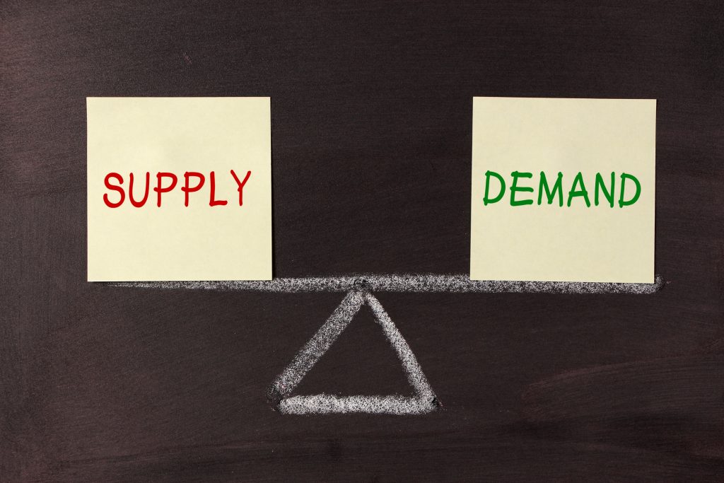Sticky notes reading supply and demand on either side of a chalk-drawn balance scale