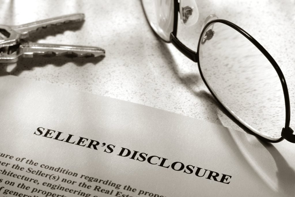 A printed seller's disclosure statement on a stone countertop, with house keys and a pair of reading glasses beside it